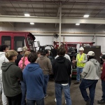 JCTC students gather by a red vehicle to listen to an R. J. Corman employee on their guided tour.